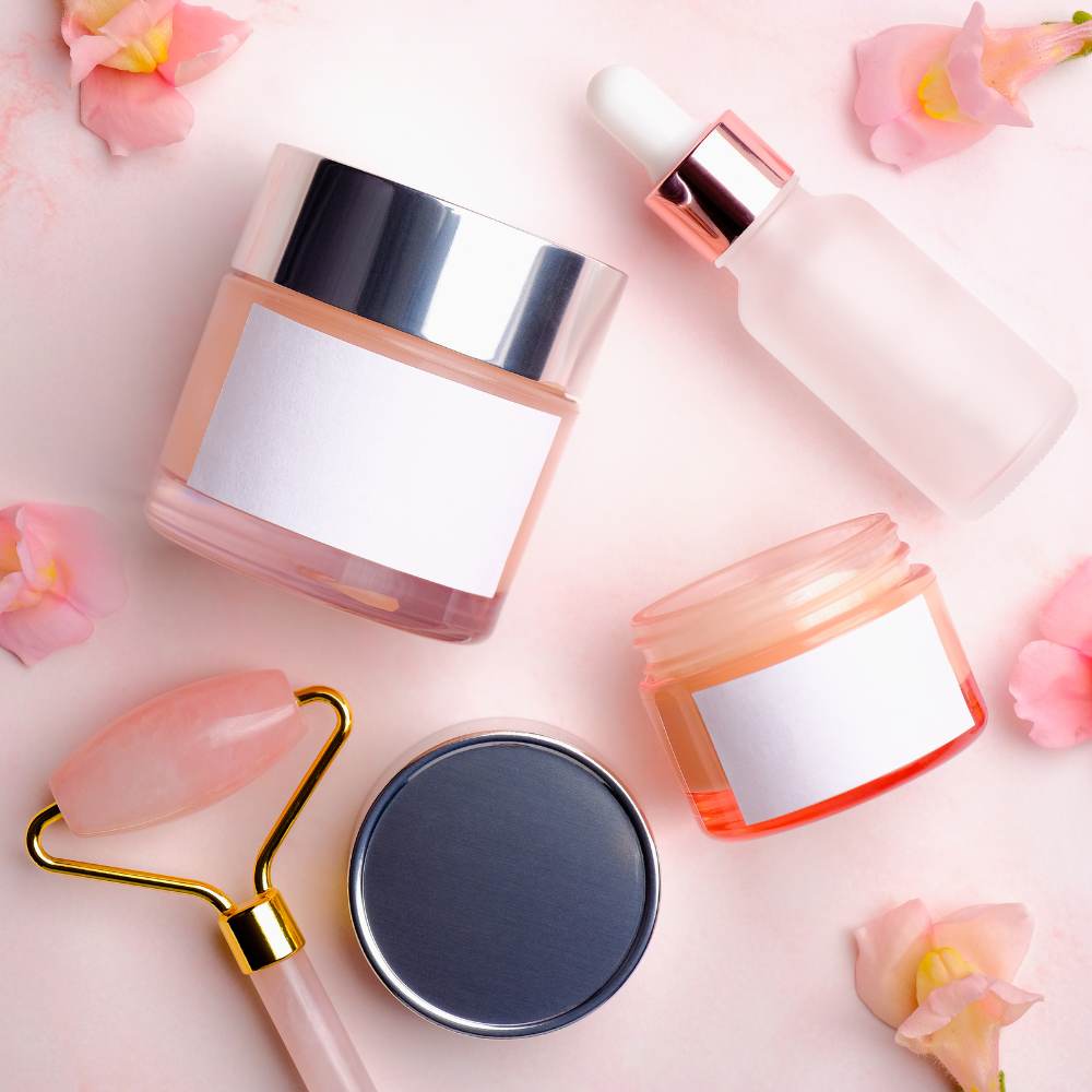 Pink skincare containers and a face roller arranged with flowers